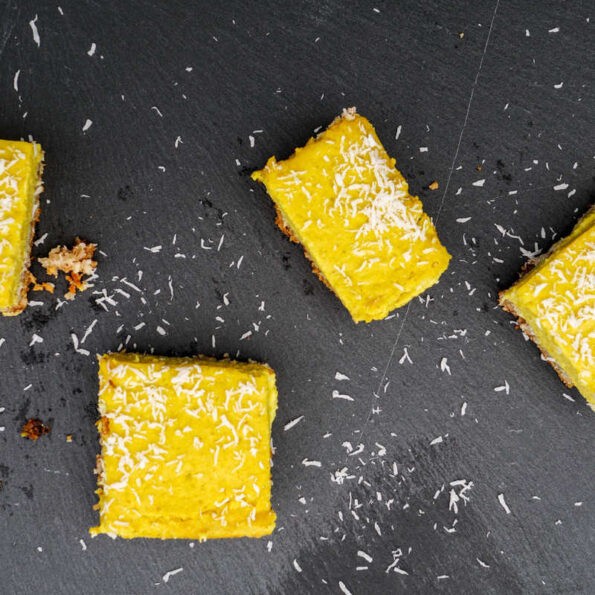 4 paleo turmeric lemon bars decorated with dessicated coconut on a black slate background
