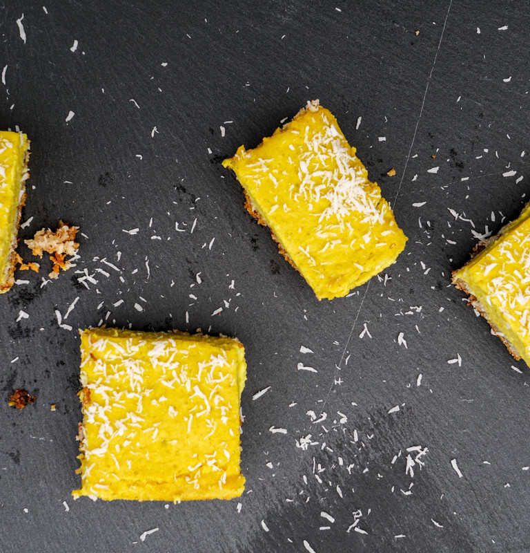 4 paleo turmeric lemon bars decorated with dessicated coconut on a black slate background