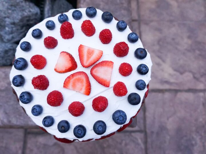 strawberries, raspberries and blue berries aranged in concentric circles on coconut whip cream on a chocolate cake near a fire pit.