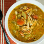 Bowl of chicken vegetables soup on burnt orange and white tablecloth and spoon