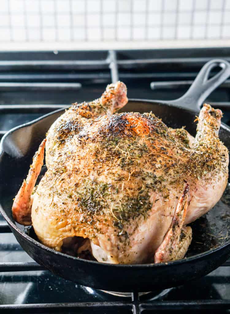 Herb coated roasted chicken in a cast iron skillet on a stove top