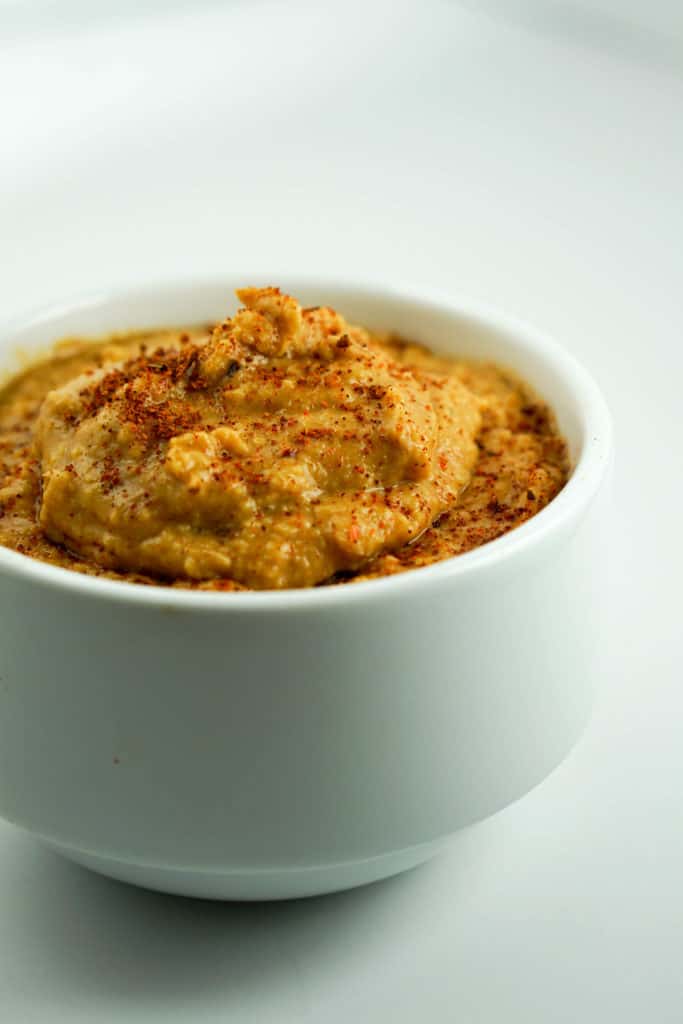 homemade hummus with paprika dusted on top in a white ramekin with white background