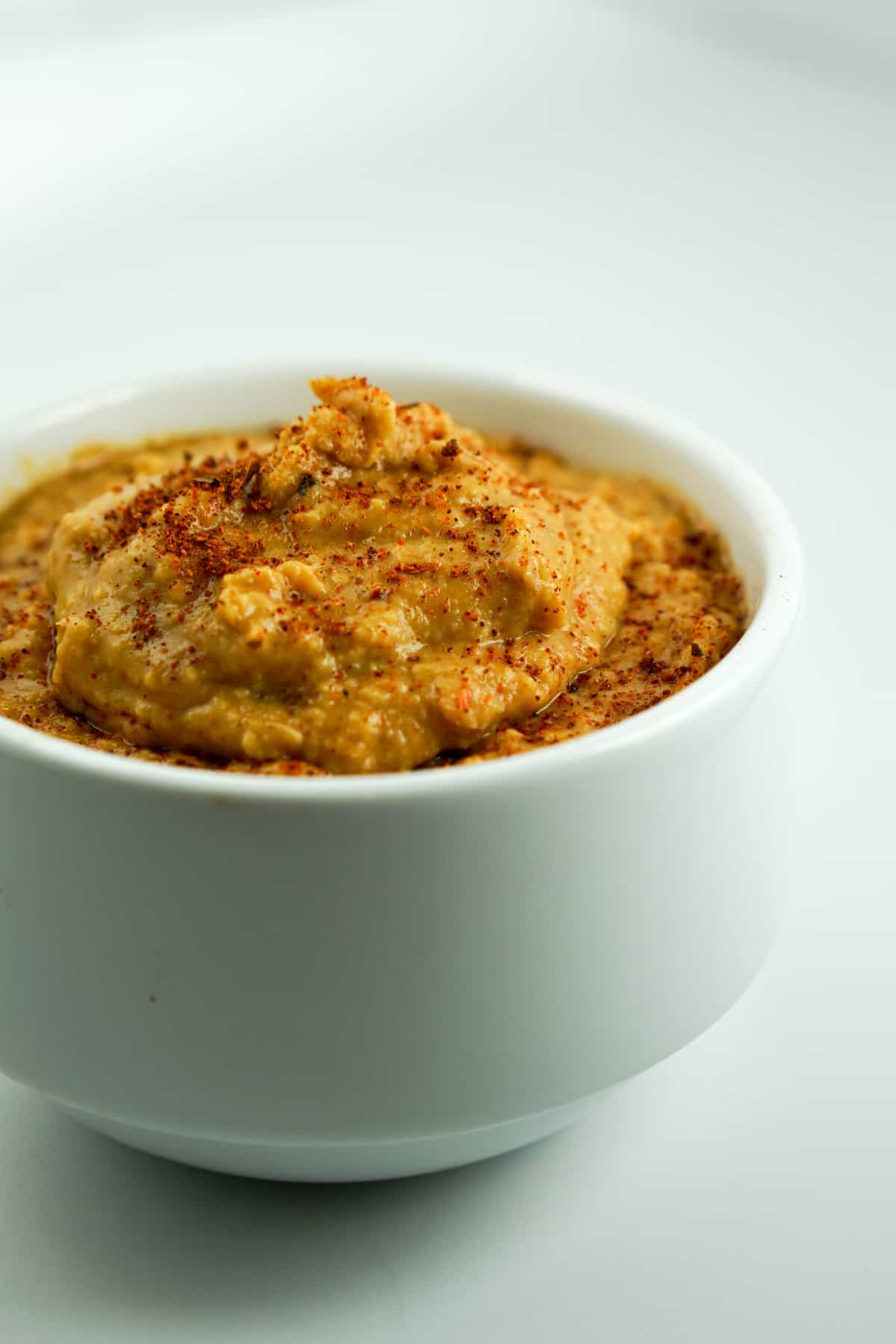 homemade hummus with paprika dusted on top in a white ramekin with white background