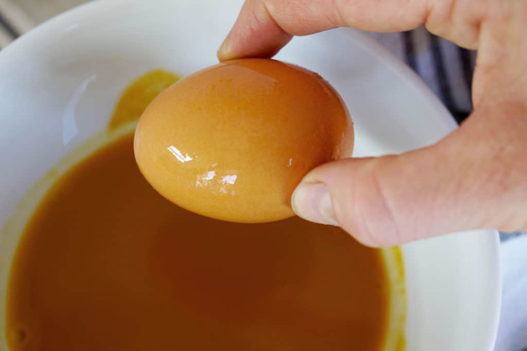Fingers grabbing a yellow dyed Easter egg over a white bowl full of natural turmeric yellow dye