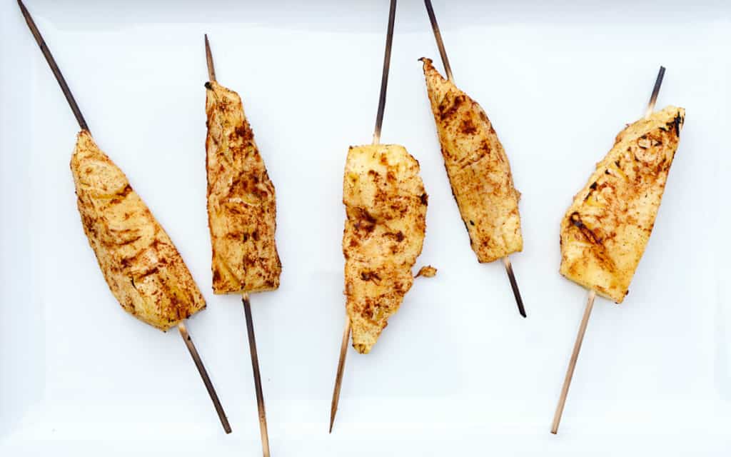 5 cinnamon dusted pineapple skewers, grilled, on white background