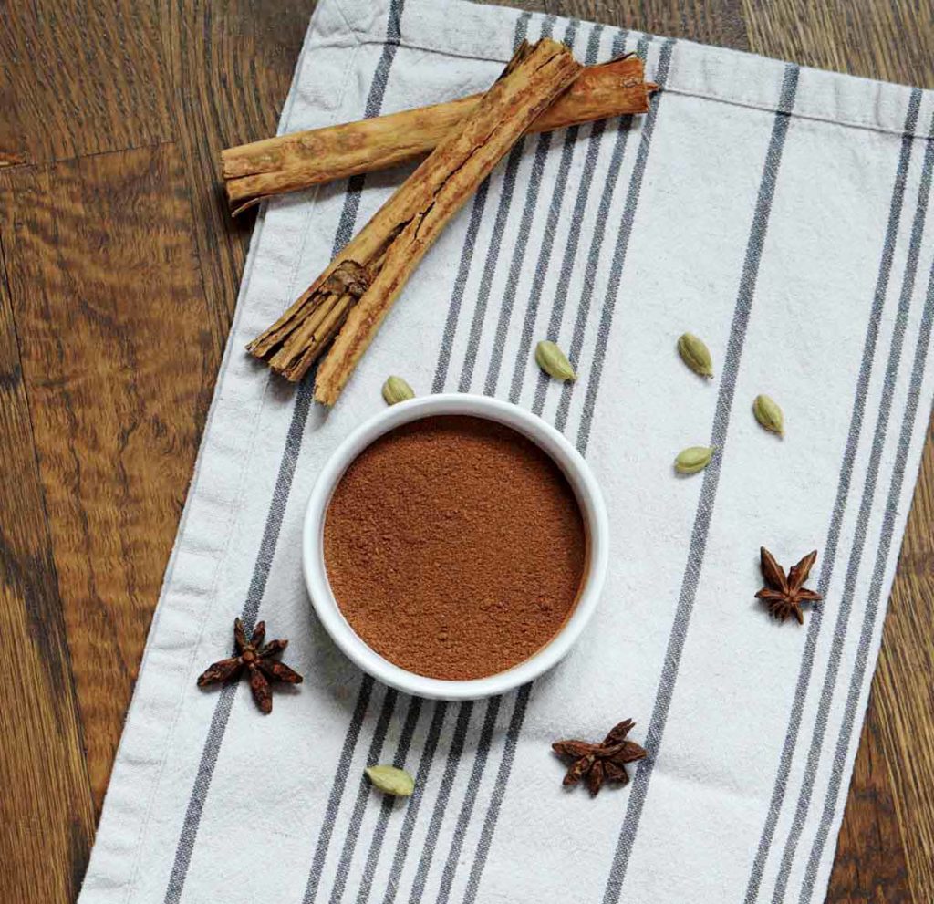 white ceramic jar of spice mix, anise, cardamom and cinnamon sticks on table