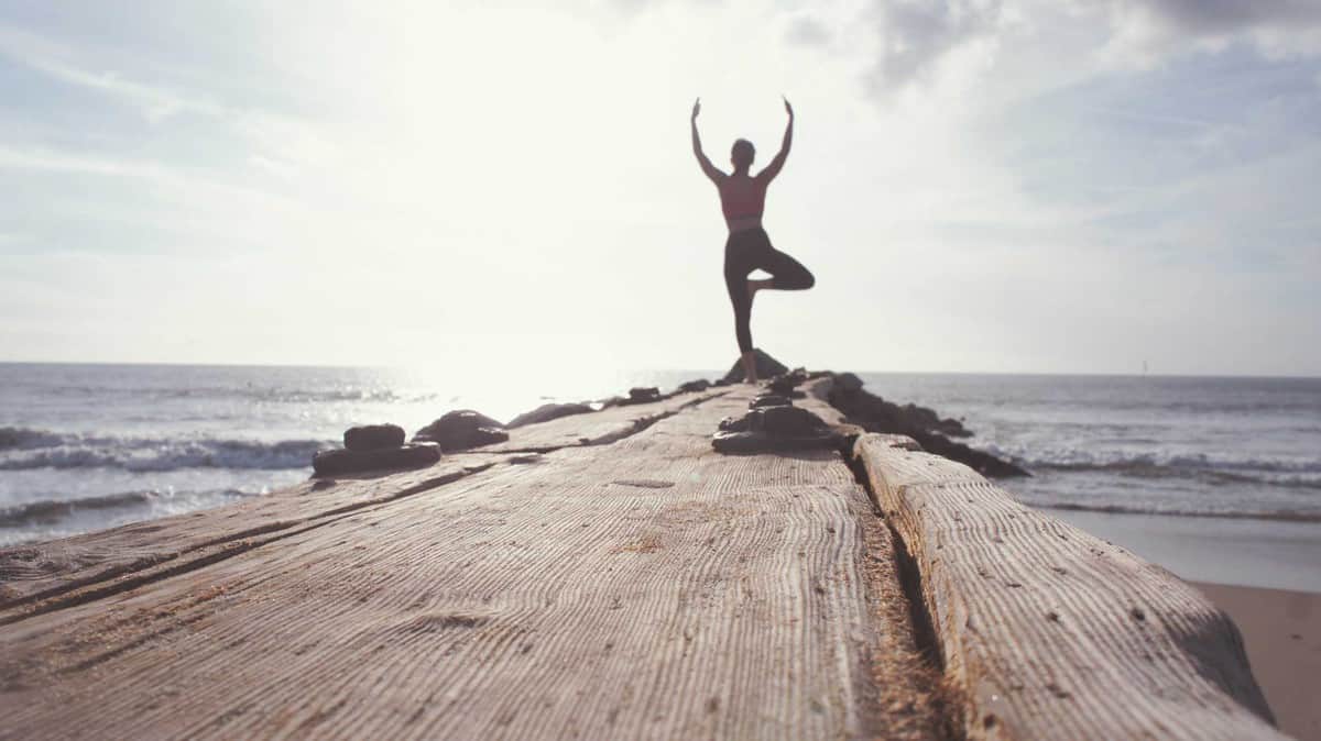 A woman doing a yoga pose looking out to the sea