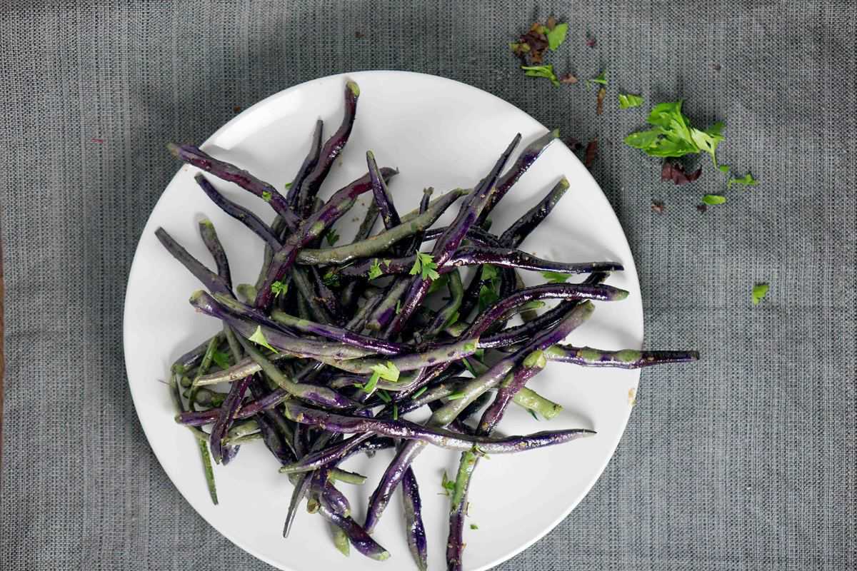 blistered purple and green beans on a white plate 