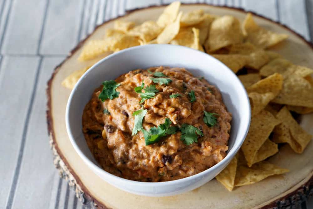 creamy chip dip in white bowl on wood serving platter with cor chips