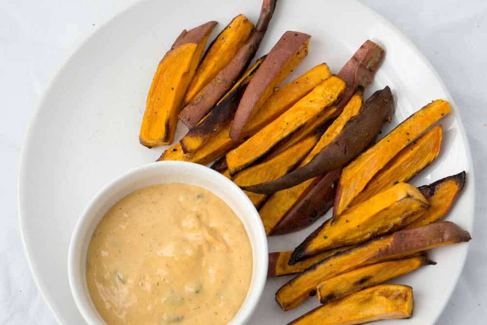 sweet potato fries in fan shape on white plate with white ramekin of spicy dairy free cashew cream sauce