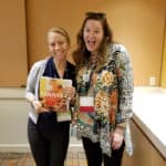 two girls standing together holding a book of kombucha recipes