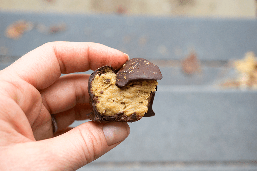 Hand holding a bitten Paleo chocolate covered pumpkin pie bites are rich and creamy, densely packed with health-supporting spices and real pumpkin, stuffed with coconut butter and doused in chocolate.