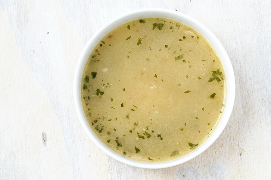 One bowl of chrsitmas goose stew. A yellow goose broth thickened with vegetables and finished with small pieces of fresh green parsley on a white table in a white bowl