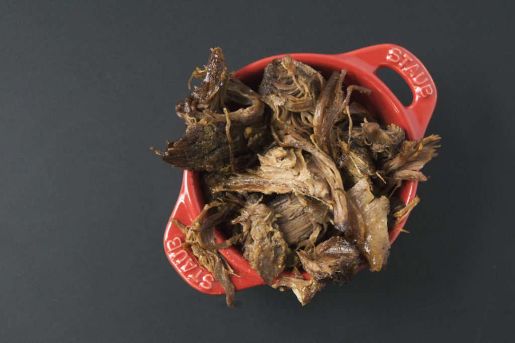Slow cooked pulled beef in red Staub ramekin on black background