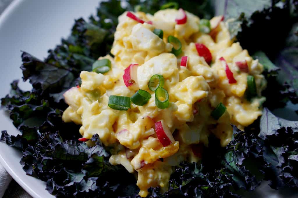 Egg salad with radish and green onion on a blue green kale leaf on a white plate