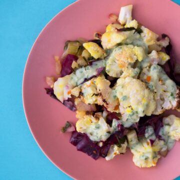 turmeric roasted cauliflower bake on bright pink plate on blue background