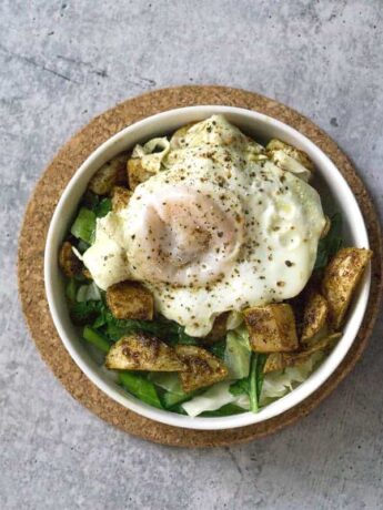 White bowl on cork circle on cement with sauteed cabbage and turnip greens with harissa roasted turnips and broth poached eggs