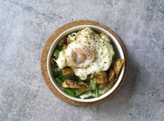 White bowl on cork circle on cement with sauteed cabbage and turnip greens with harissa roasted turnips and broth poached eggs