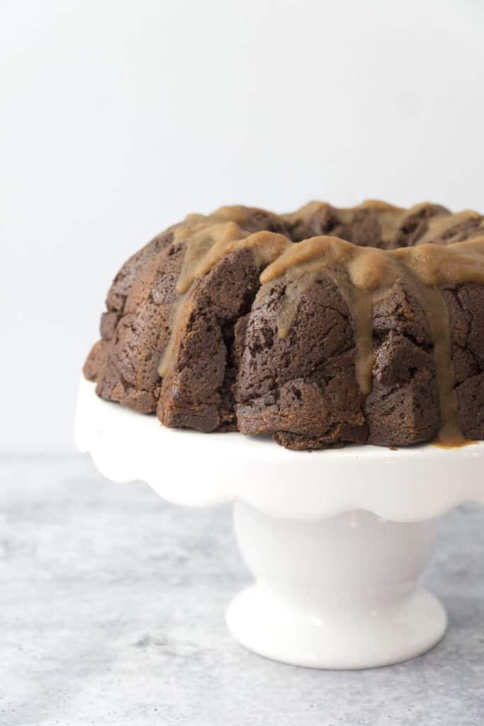 Coconut cardamom glazed chocolate chai bundt cake on white cake stand on cement table with white backdrop