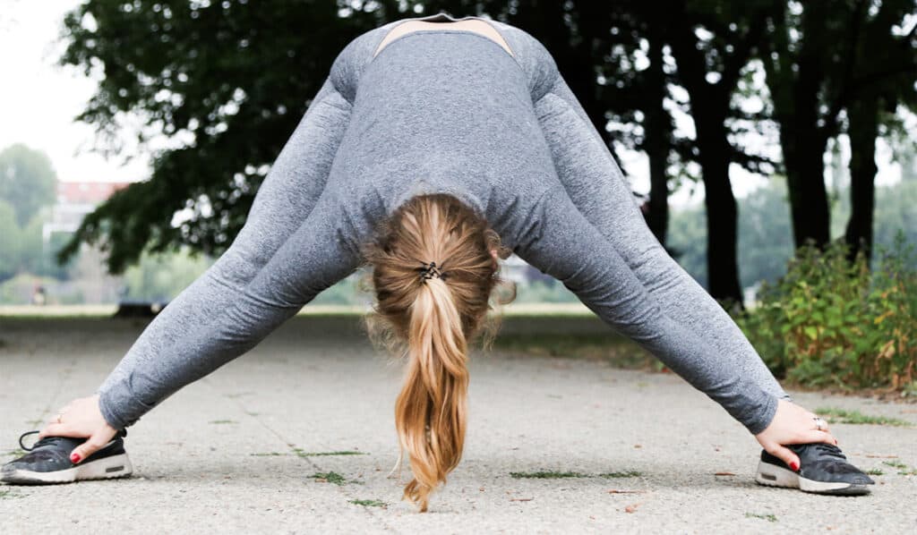 Lady in running clothes in a park stretching, getting ready to exercise to manage fat