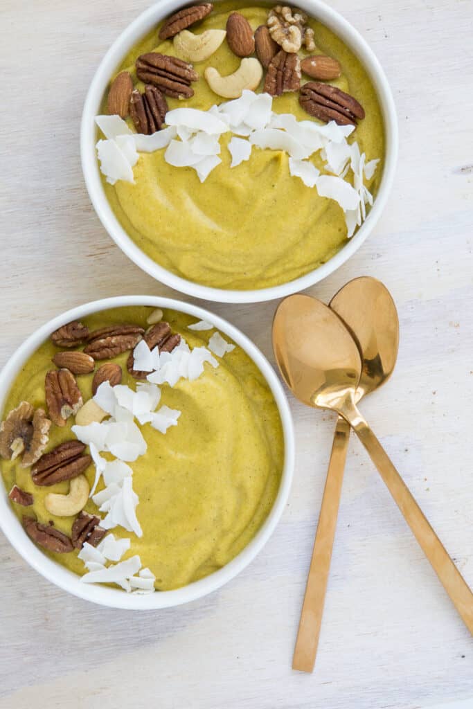Pumpkin smoothie bowl topped with roasted nuts and coconut flakes, with golden spoons