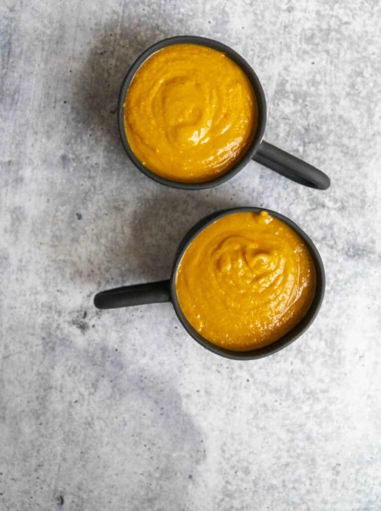 Pouring Pumpkin Thai Curry Soup in black mugs overhead