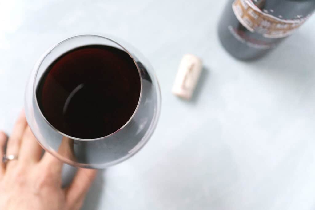 A full bulbous glass of red wine with a bottle and cork