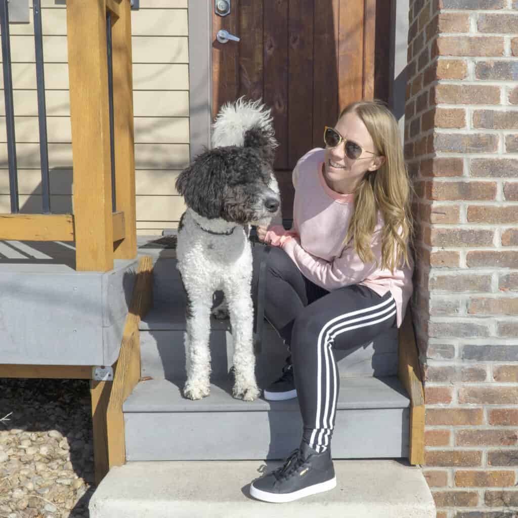 Blond girl and bernedoodle on the stairs with Adidas leggings and black sneakers and pink sweatshirt