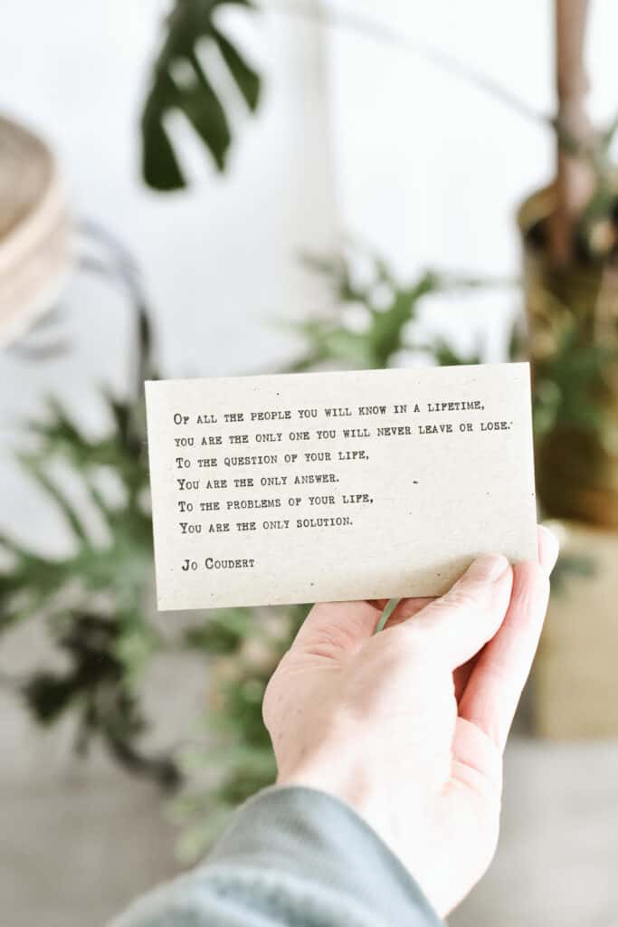 Woman's hand holding a self-love poem in plant filled living room