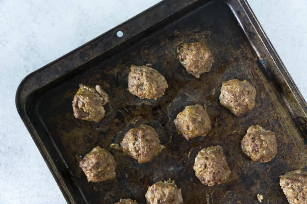 Meatballs in heavily used baking sheet on white surface