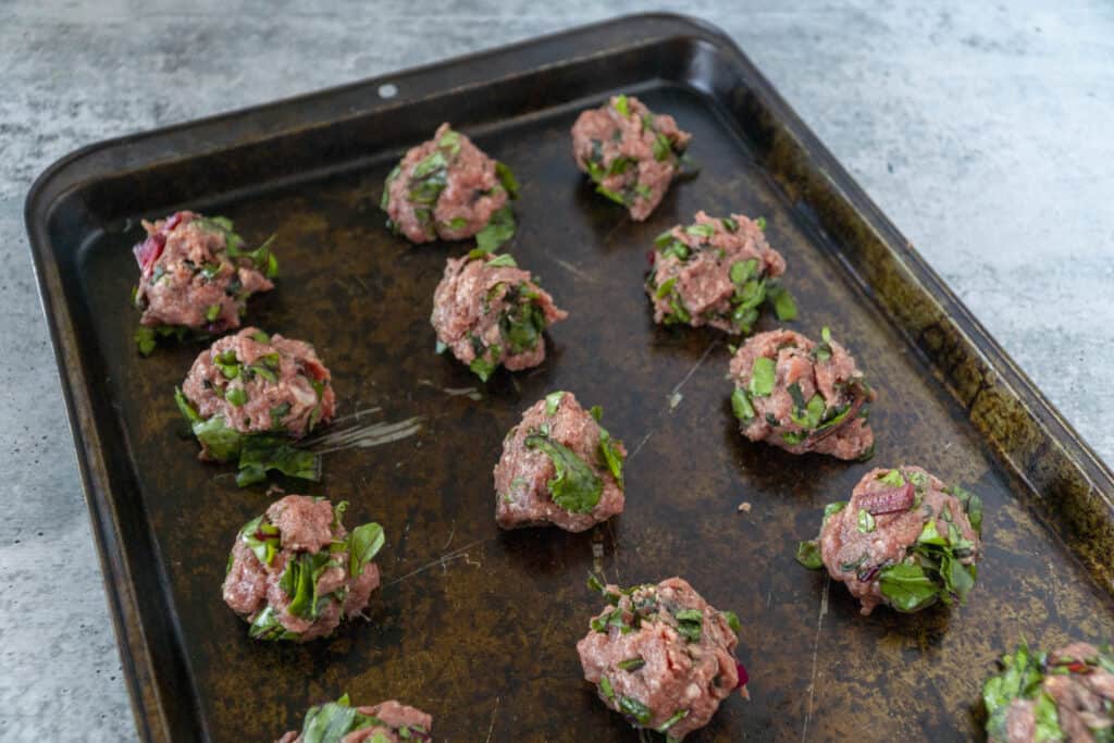 raw meatballs with beet greens mixed in on baking sheet