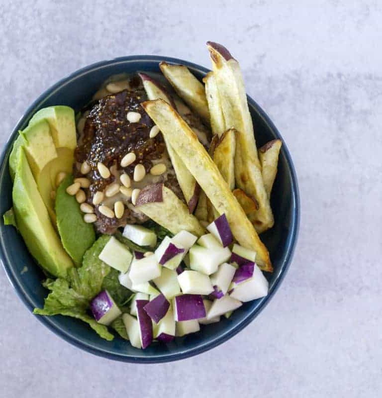 Overhead view of A hand grabs a Fig Tahini Burger bowl with sweet potato fries, kohlrabi and avocado