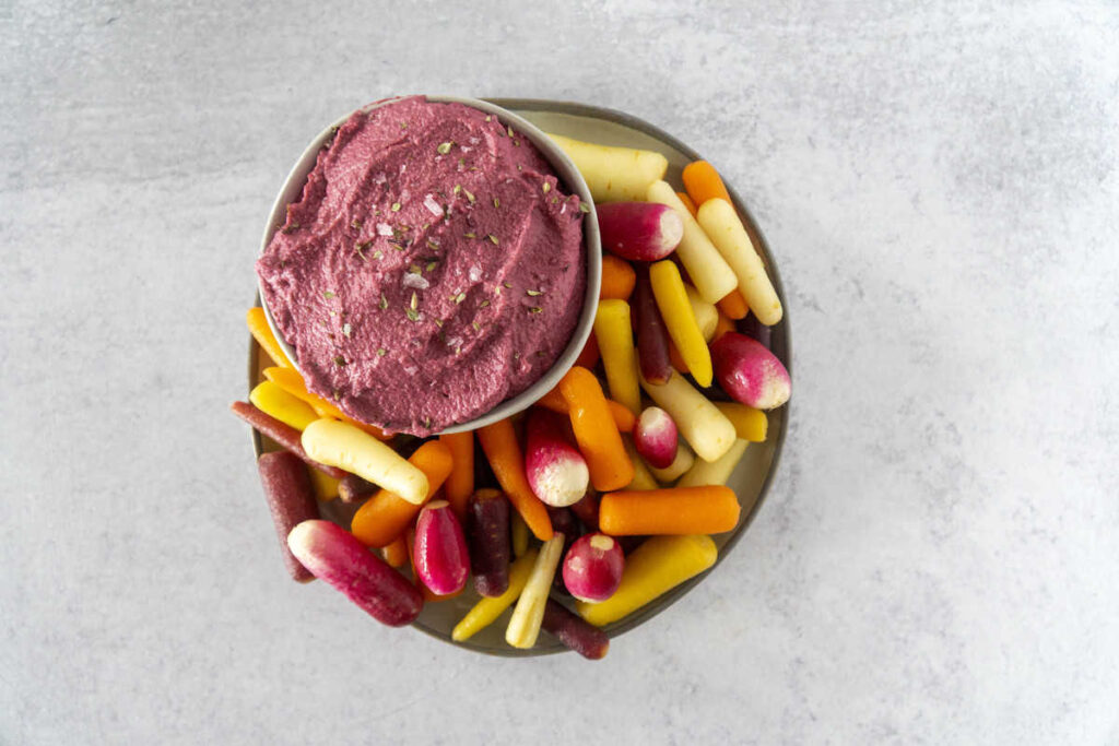 Beet hummus with rainbow carrots on concrete counter