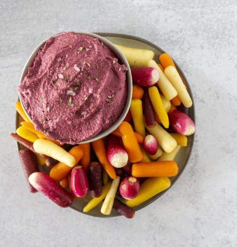 Beet hummus with rainbow carrots on concrete counter