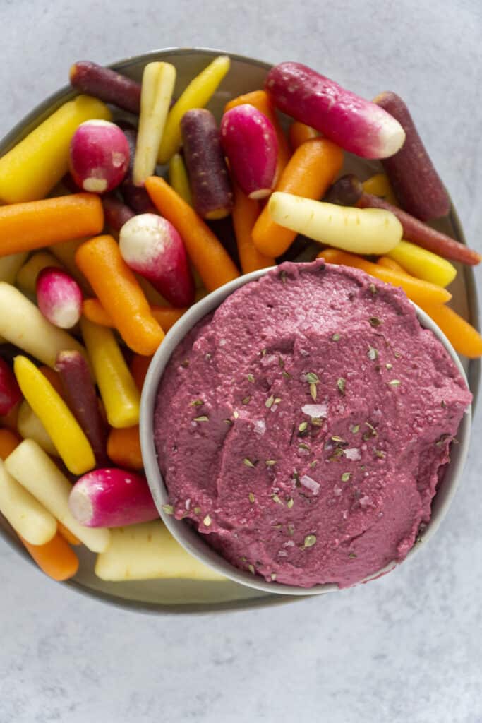 Plate of pink beet hummus with rainbow cards and radishes