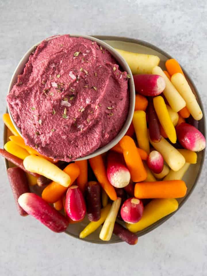 Beet hummus with rainbow carrots on concrete counter 2