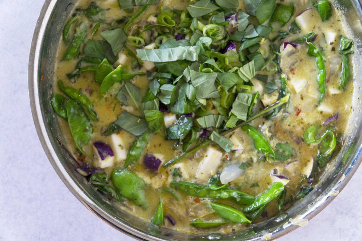 Green curry with snap peas and herbs in copper pot
