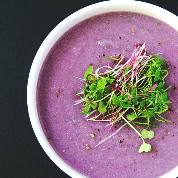 white bowl of bright purple soup with micro greens on black table