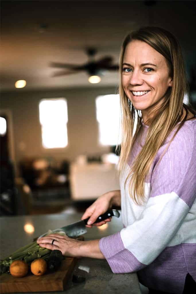 Health Coach Alicia in the kitchen, chopping food on a cutting board with living room blurred in background