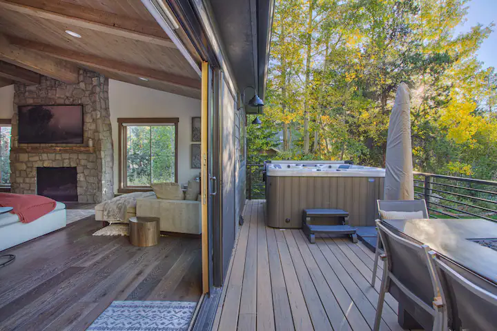Indoor outside living room with comfy couches and fire place embedded dining table next to hot tub, in front of aspens changing colors