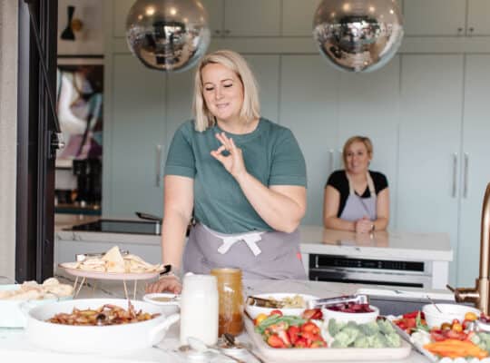 Female chef giving ok hand sign above delicious spreads of food