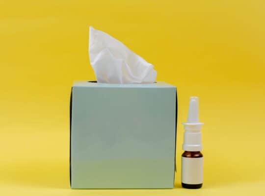 Kleenex box and nose spray in front of bright yellow background