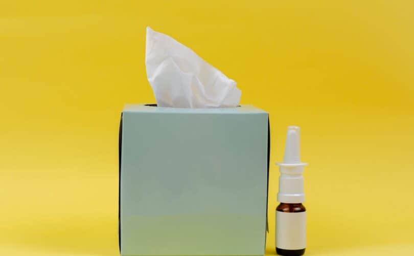 Kleenex box and nose spray in front of bright yellow background