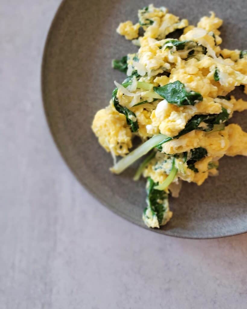 ceramic plate with pile of scrambled eggs with greens and sauerkraut in them