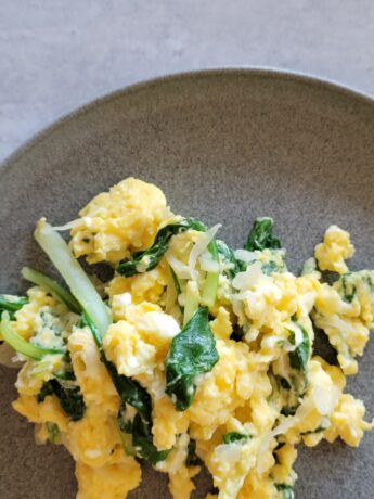 blue grey plate with a pile of scrambled eggs on top - eggs have spinach and greens in them